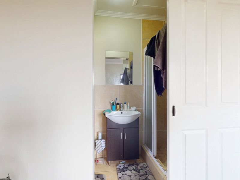 A compact bathroom featuring a vanity cabinet with a ceramic basin, a shower enclosure, and neutral wall tiling.