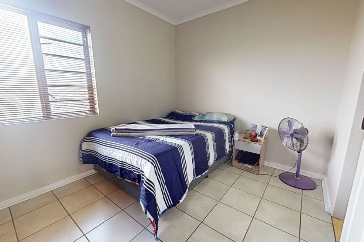 A functional bedroom featuring tiled flooring, neutral wall finishes, and a window fitted with venetian blinds.