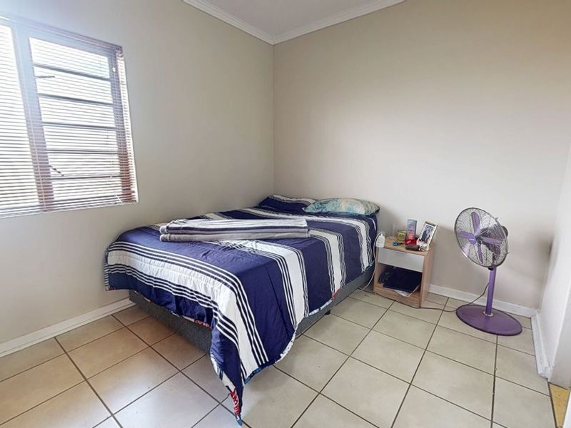 A functional bedroom featuring tiled flooring, neutral wall finishes, and a window fitted with venetian blinds.
