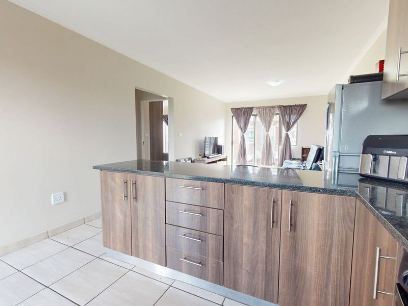 Open plan kitchen and living area featuring modern wood cabinetry, granite countertops, tiled flooring, and access to a balcony through sliding glass doors.