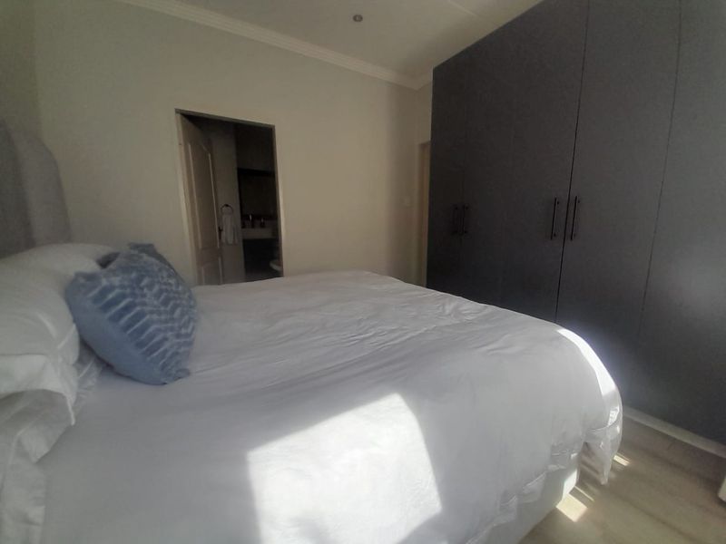 A well-maintained bedroom featuring dark built-in cupboards, recessed downlighting, and coving, with an adjoining bathroom visible through the doorway.