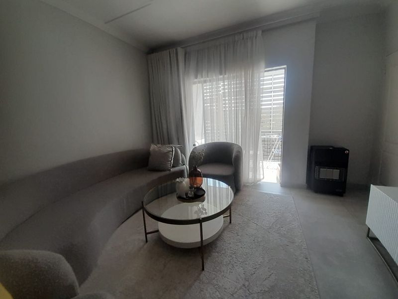 A well-lit living room featuring neutral tiled flooring and a large sliding glass door providing access to an outdoor balcony area.