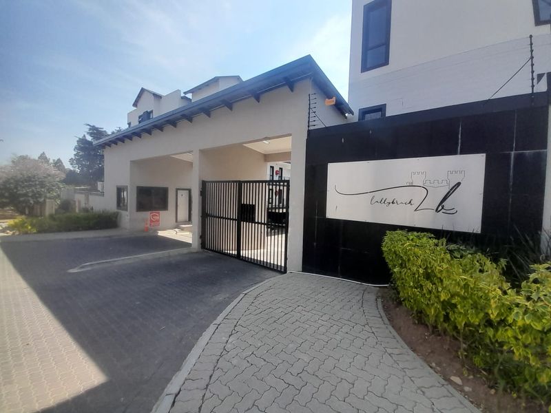 The entrance to Lallybroch complex featuring a secure gated access point, paved driveway, and perimeter electric fencing.