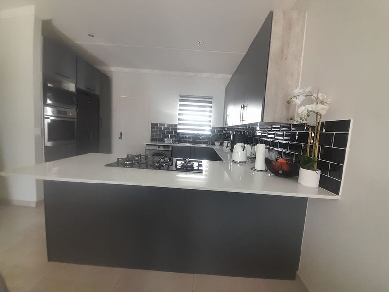 Modern kitchen featuring dark cabinetry, contrasting white quartz countertops, a gas hob, and a stylish black subway tile backsplash.