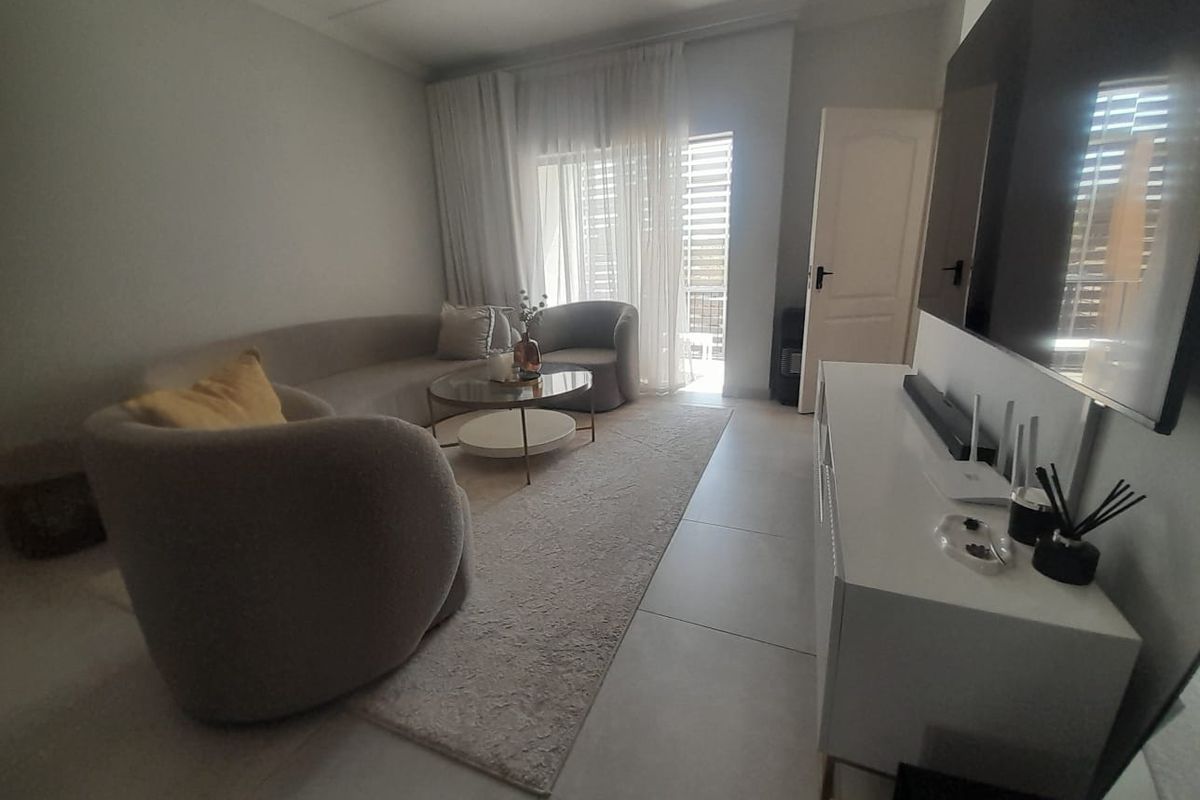 A bright and modern living room featuring large format floor tiles, recessed ceiling lighting, and a sliding glass door providing access to the balcony.