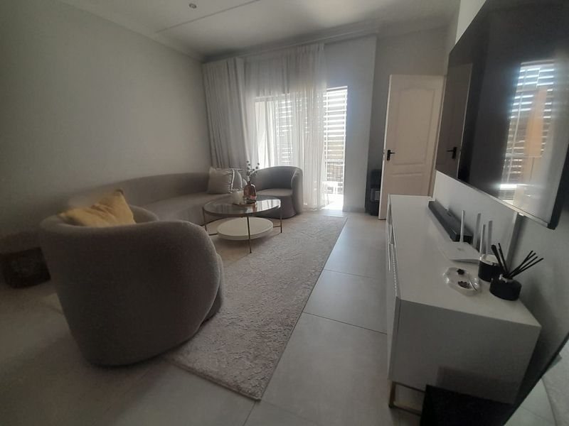 A bright and modern living room featuring large format floor tiles, recessed ceiling lighting, and a sliding glass door providing access to the balcony.
