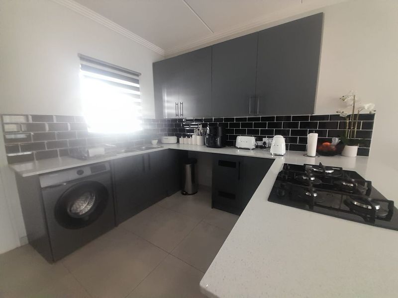 Modern kitchen featuring dark grey cabinetry, contrasting subway tile backsplash, stone countertops, and a built-in gas hob with an integrated washing machine.