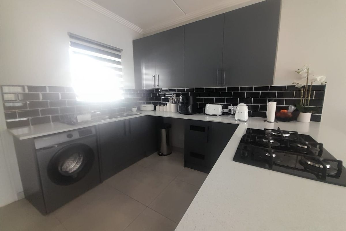 Modern kitchen featuring dark grey cabinetry, contrasting subway tile backsplash, stone countertops, and a built-in gas hob with an integrated washing machine.