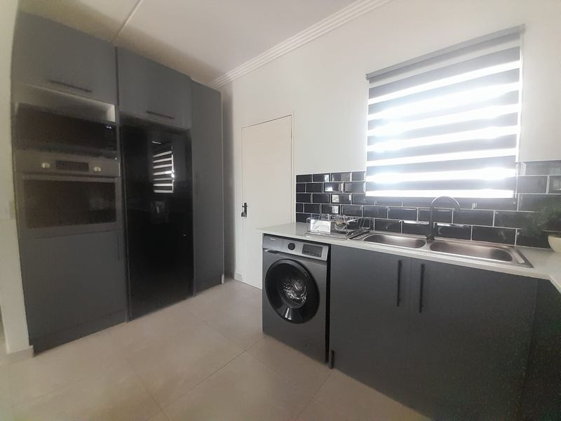 Modern laundry room featuring dark grey cabinetry, double sink, black subway tile backsplash, built-in oven, and integrated microwave with tiled flooring.
