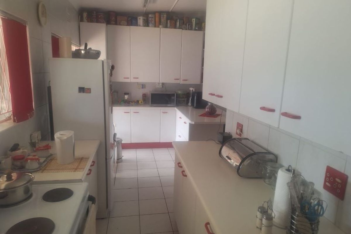 A functional kitchen featuring white cabinetry, laminate countertops, and tiled flooring, providing a practical workspace with integrated stove and microwave.