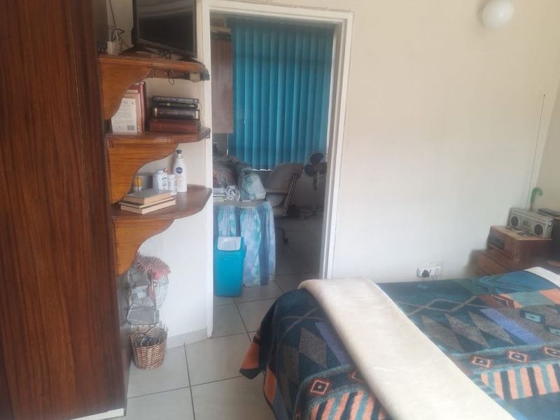 A bedroom featuring tiled flooring and built-in shelving, with an adjacent room visible through the doorway.