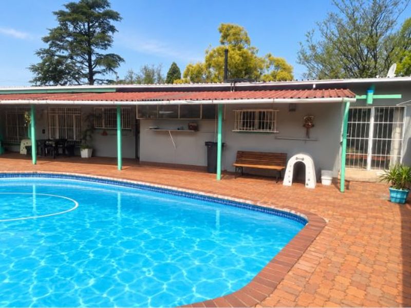 Outdoor pool area featuring a large swimming pool, brick paved surround, and a covered patio area with security bars on windows.