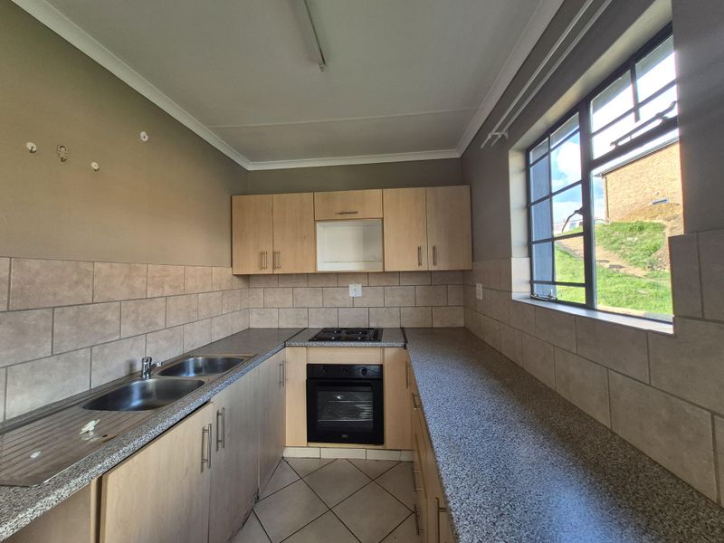 A functional kitchen featuring light wood cabinetry, granite-look laminate countertops, a built-in oven with gas hob, and neutral ceramic wall and floor tiling.
