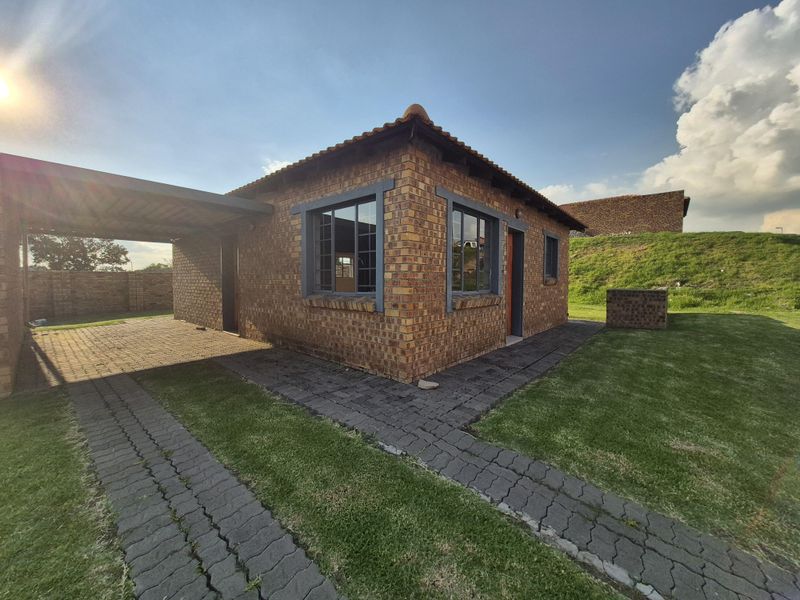 A well-maintained face brick townhouse featuring a private carport, paved driveway, and established lawn area.