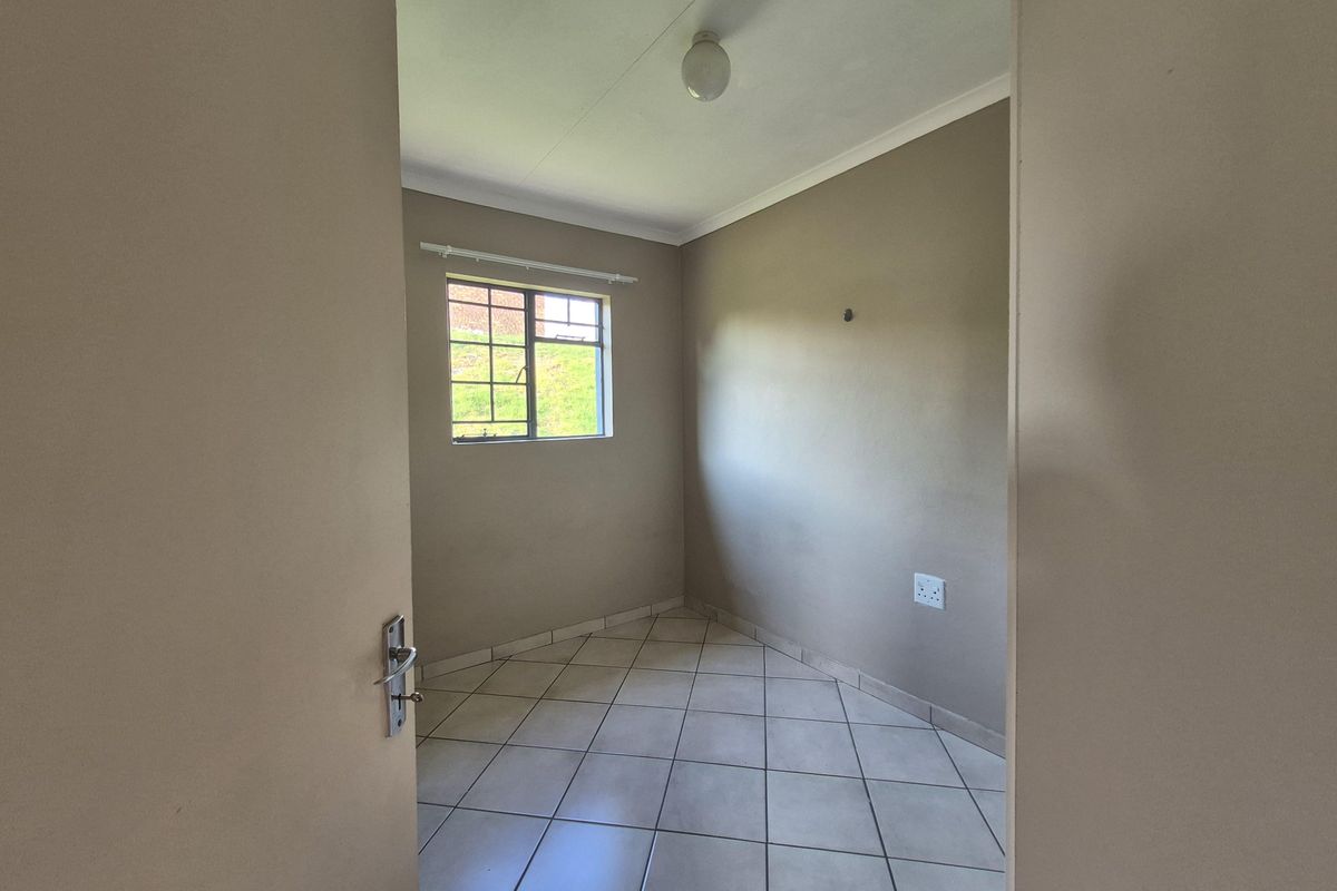 A clean, empty bedroom featuring neutral wall tones, tiled flooring, and a window with security bars, offering a blank canvas for personalization.
