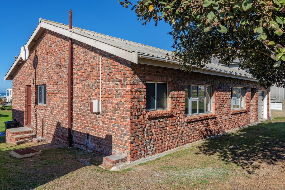 A side and rear view of a face brick house featuring a corrugated metal roof and aluminium window frames set within a garden area.