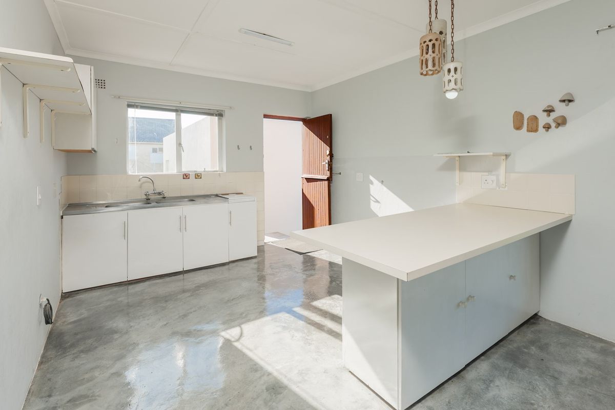 A functional, empty kitchen featuring polished concrete floors, built-in cabinetry, a stainless steel sink, and a breakfast counter, offering a clean slate for renovation.