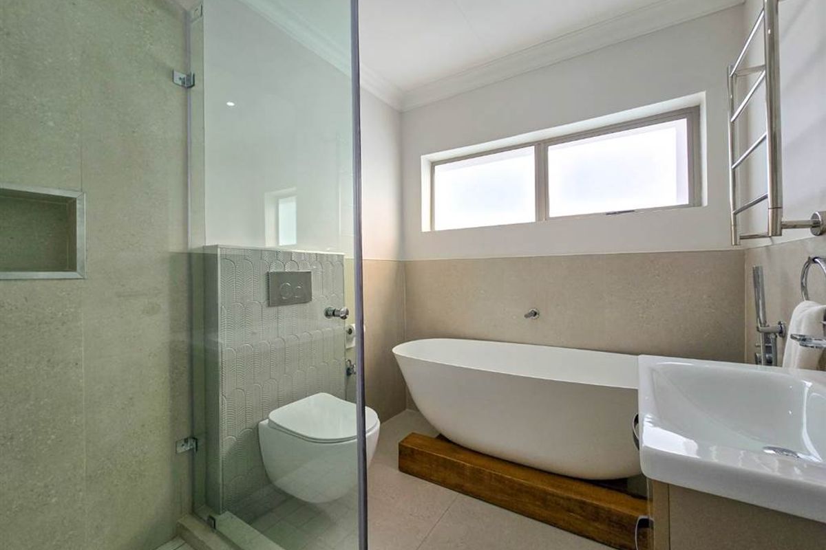 Modern bathroom featuring a freestanding bathtub, wall-hung toilet with concealed cistern, glass-enclosed shower with niche, and a heated towel rail.
