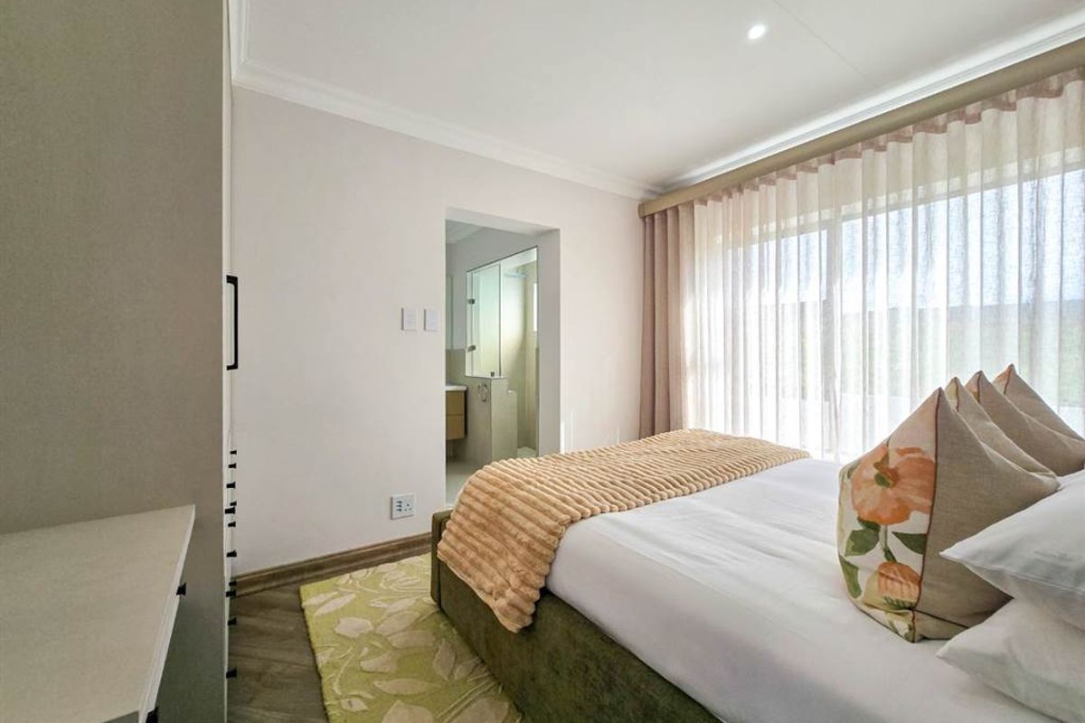 A well-maintained bedroom featuring built-in wardrobes, recessed lighting, and a sliding glass door leading to an en-suite bathroom.
