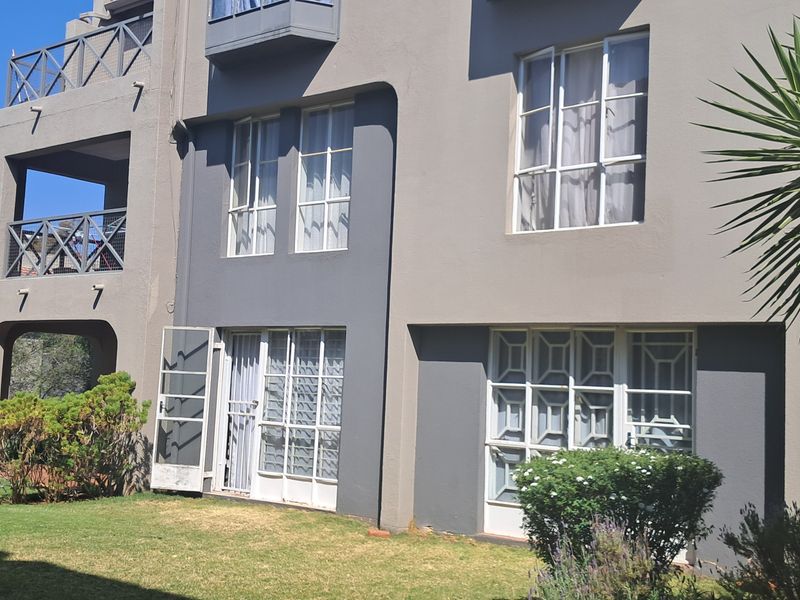 Rear view of a multi-story apartment building featuring balconies, security gates, and casement windows overlooking a private garden area.