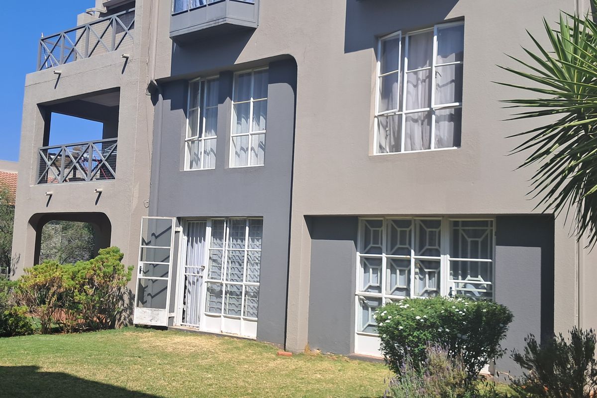 Rear view of a multi-story apartment building featuring balconies, security gates, and casement windows overlooking a private garden area.