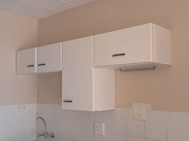 A functional kitchen area featuring white wall-mounted cabinetry, a tiled backsplash, and a sink faucet, presenting a clean but dated aesthetic.