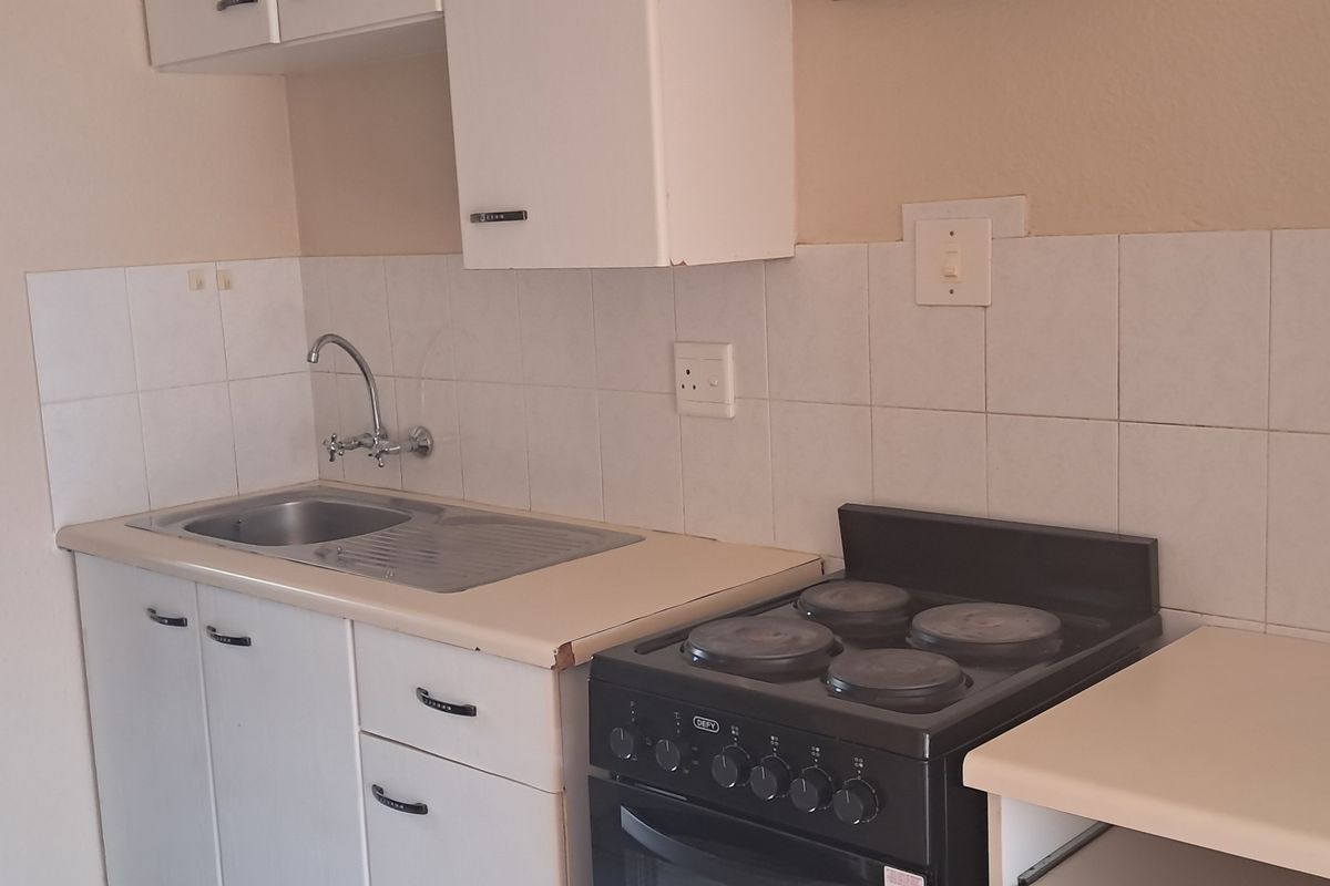 A functional kitchen featuring a stainless steel sink, laminate countertops, tiled backsplash, and a freestanding electric stove with built-in cabinetry.