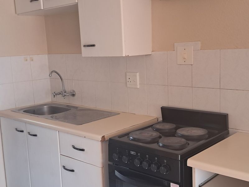 A functional kitchen featuring a stainless steel sink, laminate countertops, tiled backsplash, and a freestanding electric stove with built-in cabinetry.