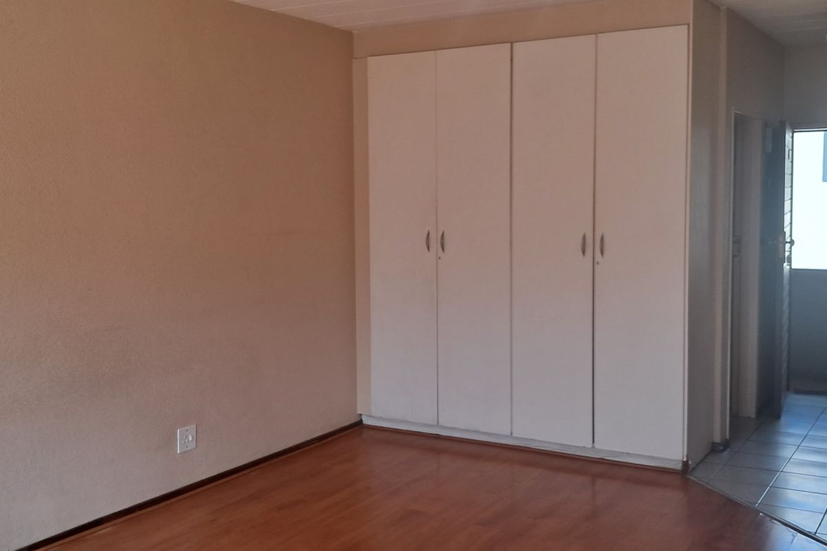 A spacious bedroom featuring laminate flooring, built-in cupboards, and direct access to a tiled hallway leading to the exterior entrance.
