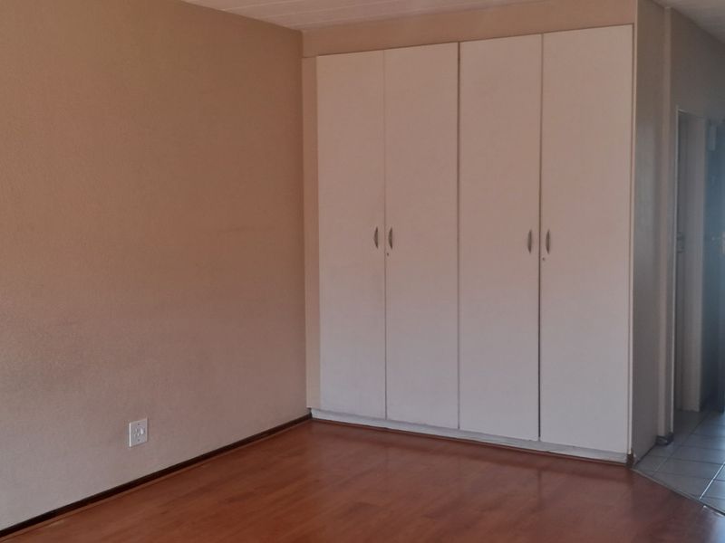 A spacious bedroom featuring laminate flooring, built-in cupboards, and direct access to a tiled hallway leading to the exterior entrance.