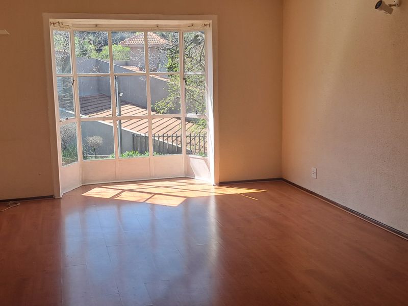 An empty living room featuring laminate flooring, a large bay window providing natural light, and built-in cabinetry.