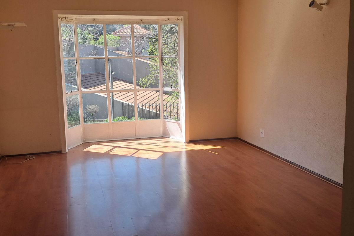 An empty living room featuring laminate flooring, a large bay window providing natural light, and built-in cabinetry.