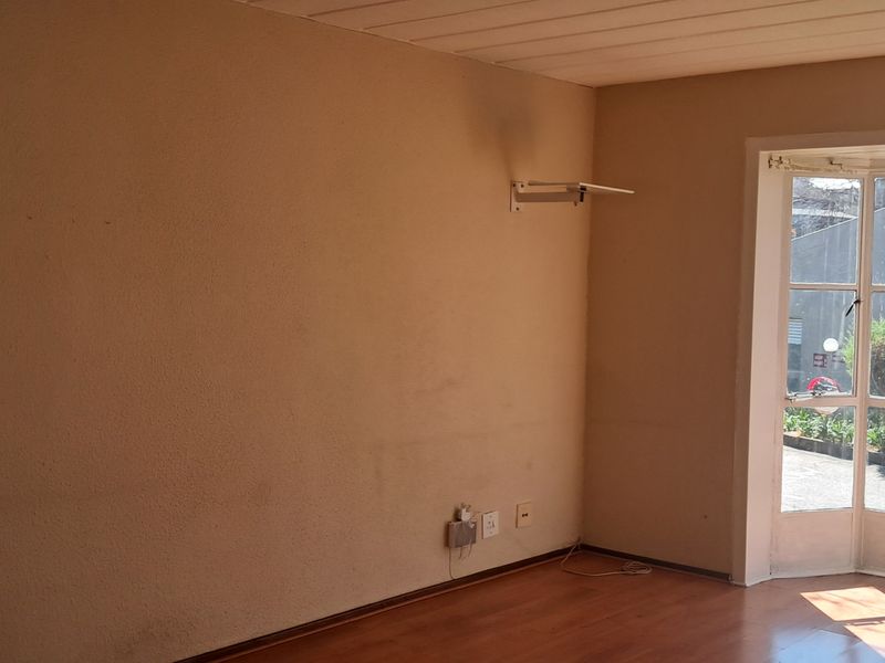 An empty living room featuring laminate flooring and a large bay window, providing natural light and a view of the exterior.