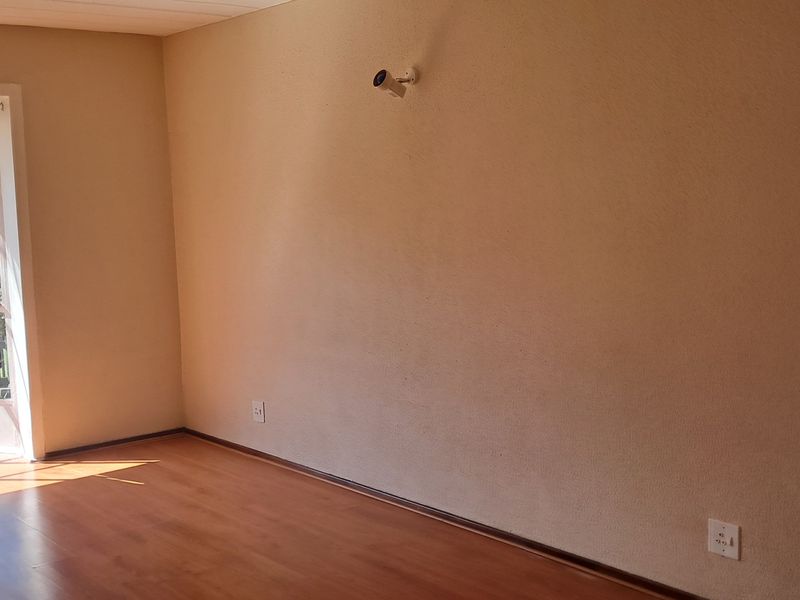 An empty living room featuring laminate flooring, a large window providing natural light, and a wall-mounted security camera.