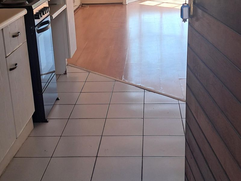 Open-plan kitchen and living area featuring a mix of tiled and laminate flooring, built-in cabinetry, and access to an outdoor space via french doors.