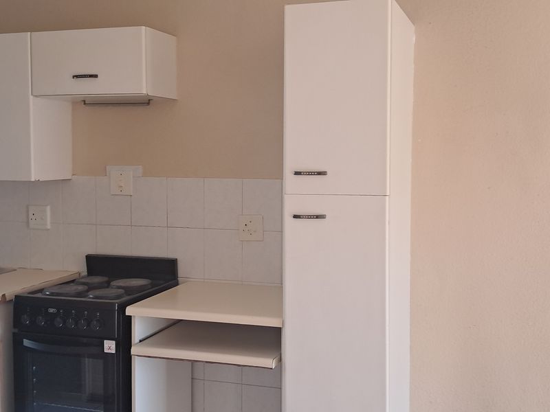 A functional kitchen featuring white built-in cabinetry, a tiled backsplash, a stainless steel sink, and a freestanding stove with a tall pantry unit.