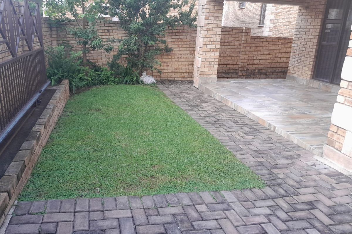 A private rear courtyard featuring a covered patio, paved flooring, and a small lawn area enclosed by brick boundary walls.