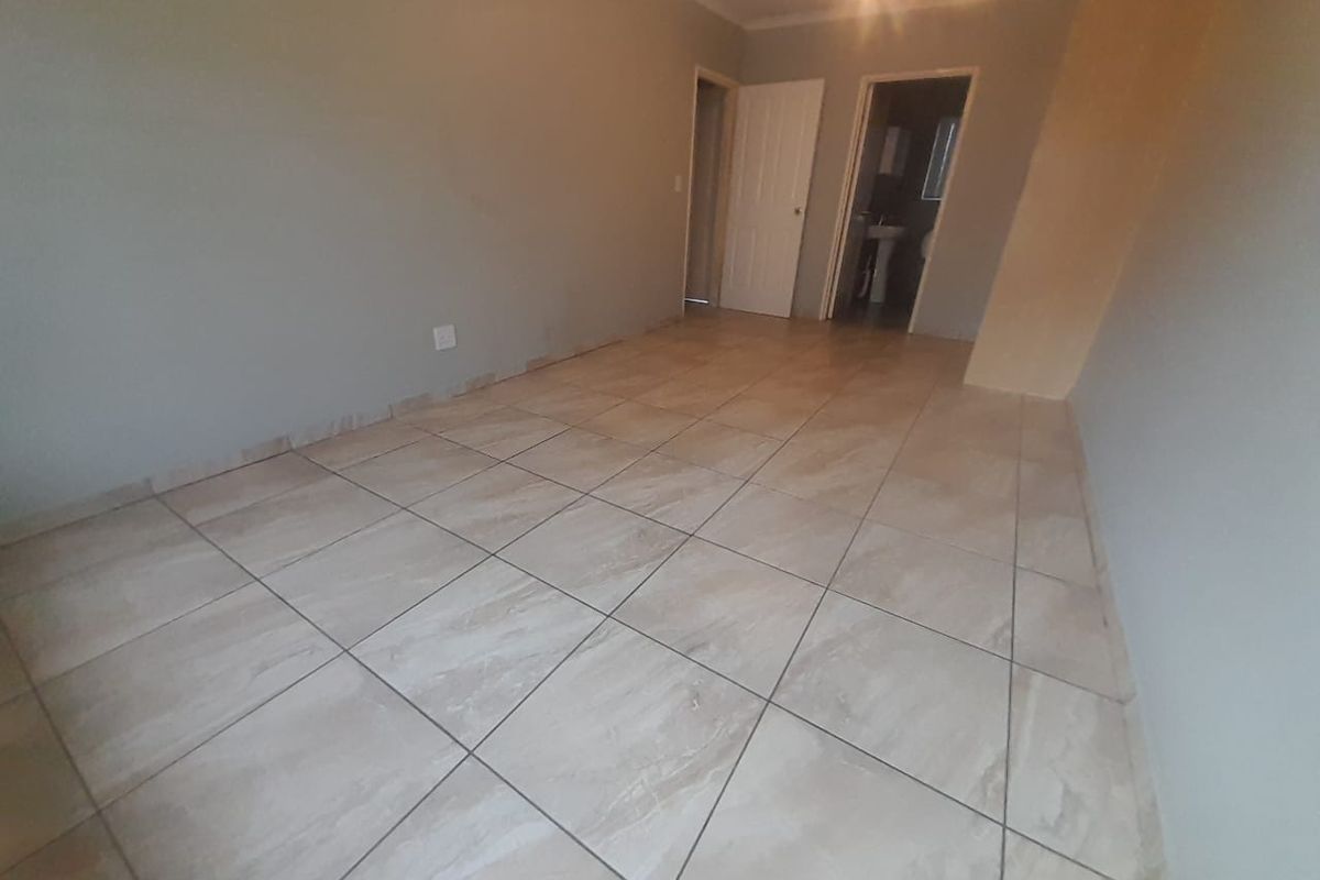 An empty bedroom featuring neutral wall paint, tiled flooring, and access to an adjoining bathroom.