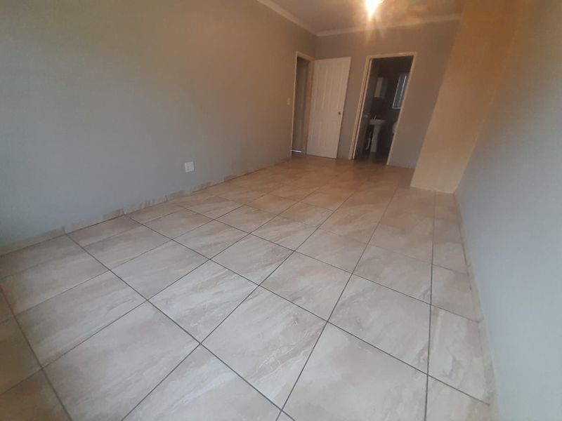 An empty bedroom featuring neutral wall paint, tiled flooring, and access to an adjoining bathroom.