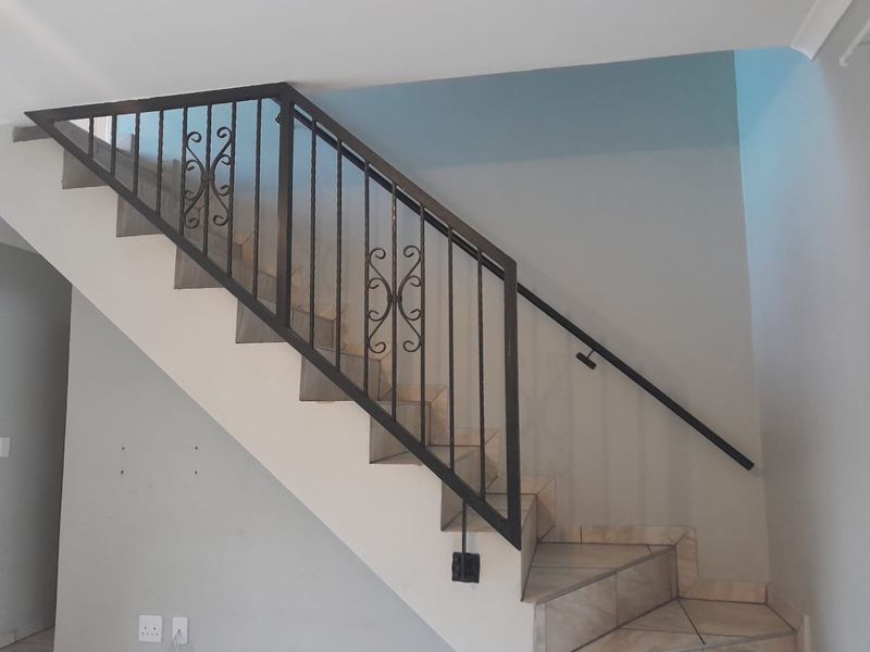 A staircase featuring a decorative wrought iron railing and tiled steps, situated in an open hallway area.