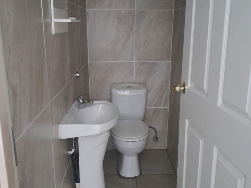 A compact, modern guest bathroom featuring neutral wall and floor tiles, a pedestal basin, and a standard toilet.