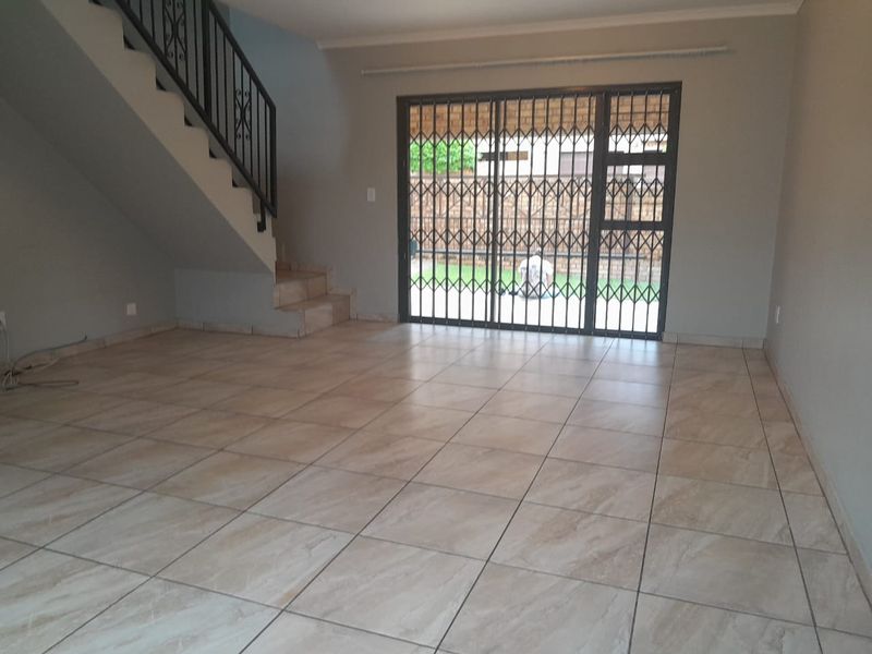Spacious open-plan living area featuring neutral tiled flooring, a staircase with a metal balustrade, and a sliding glass door leading to the rear garden.