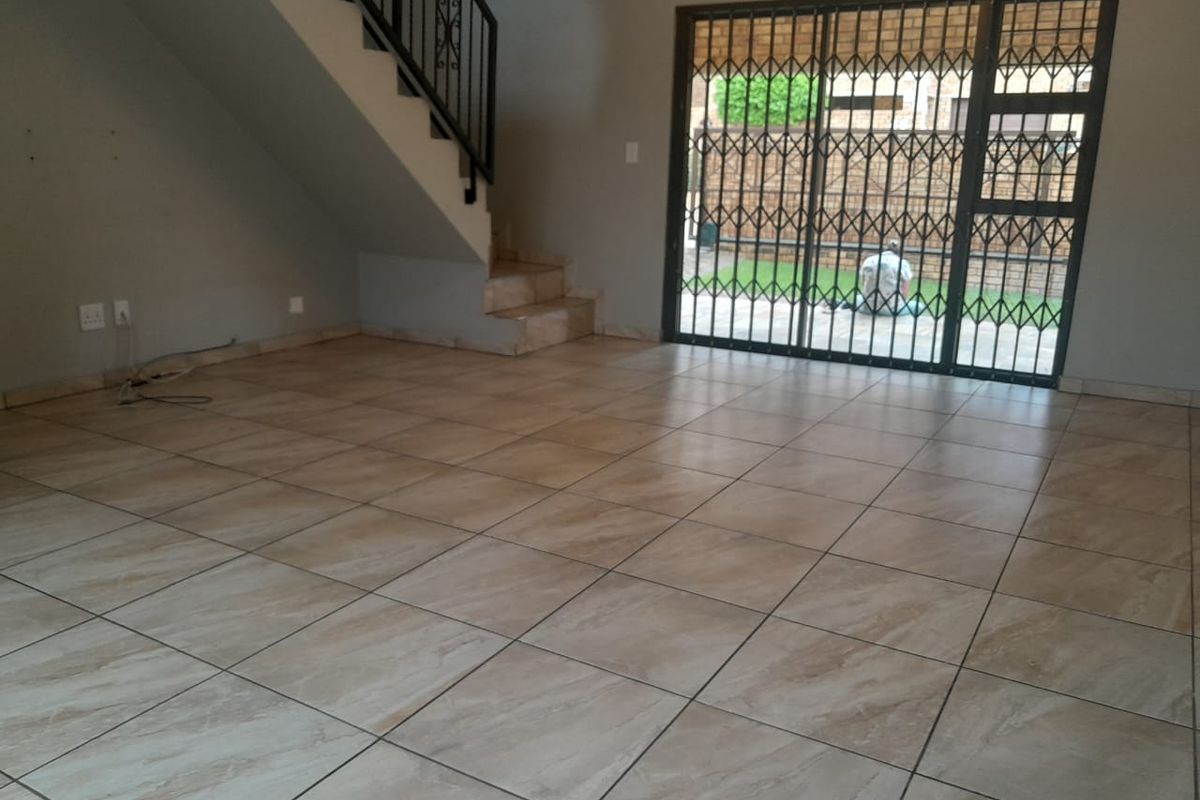 An empty, open-plan living area featuring neutral floor tiles, a staircase with a metal railing, and a sliding door leading to the exterior.