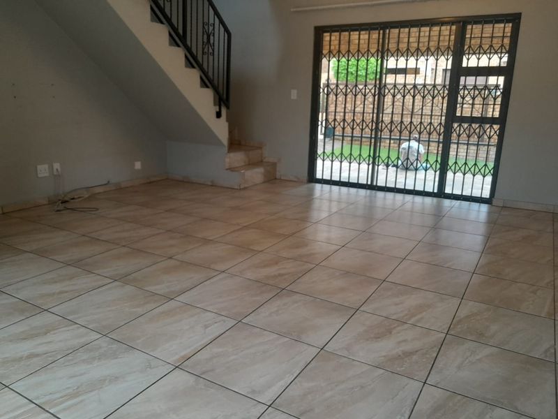 An empty, open-plan living area featuring neutral floor tiles, a staircase with a metal railing, and a sliding door leading to the exterior.