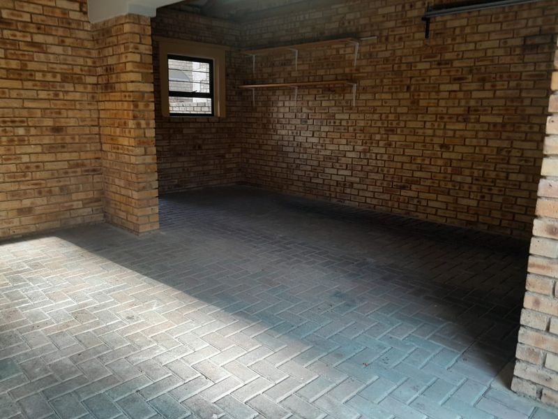 A spacious, empty garage featuring exposed brick walls, durable herringbone brick flooring, and a window with security bars.