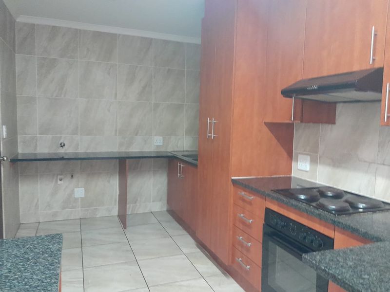 A functional kitchen featuring wood-finish cabinetry, granite countertops, a built-in oven with hob, and neutral tiled splashbacks and flooring.