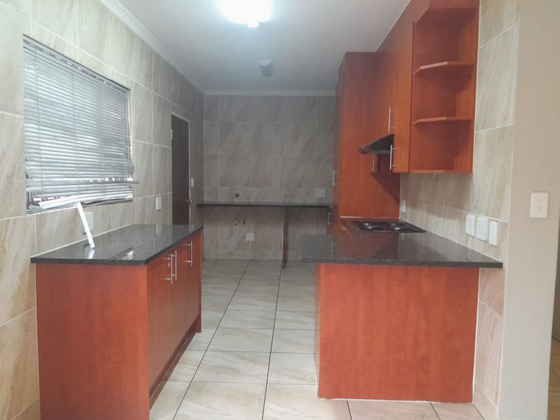 A functional kitchen featuring granite countertops, built-in wooden cabinetry, a hob with extractor fan, and neutral tiled finishes throughout.