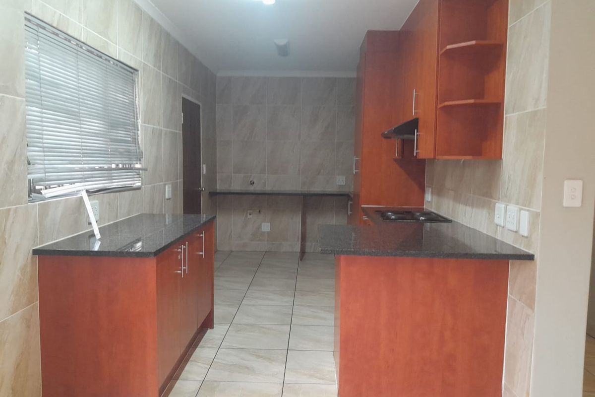 A functional kitchen featuring granite countertops, built-in wooden cabinetry, a hob with extractor fan, and neutral tiled finishes throughout.