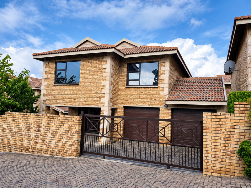Front elevation of a double-storey townhouse featuring a brick facade, tiled roof, double garage, and a secure metal driveway gate.