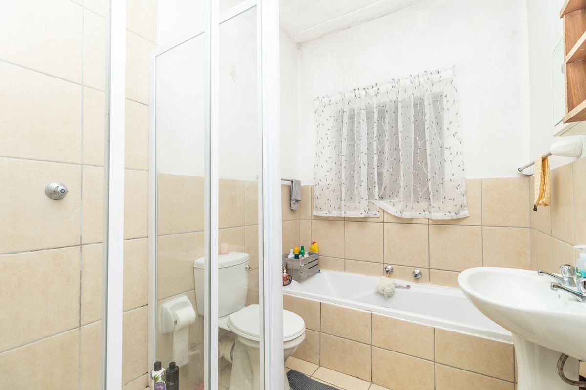A functional bathroom featuring a shower enclosure, bathtub, pedestal basin, and toilet with neutral wall tiling.